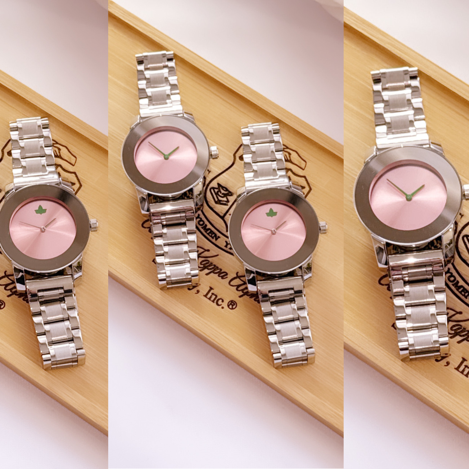 The image shows a series of silver metal wristwatches with a pink watch face, featuring a small green ivy leaf detail at the top of the watch face. The watches are displayed on a bamboo surface engraved with a logo and text related to Alpha Kappa Alpha Sorority, Inc. The composition highlights the watch's elegant and minimalistic design.